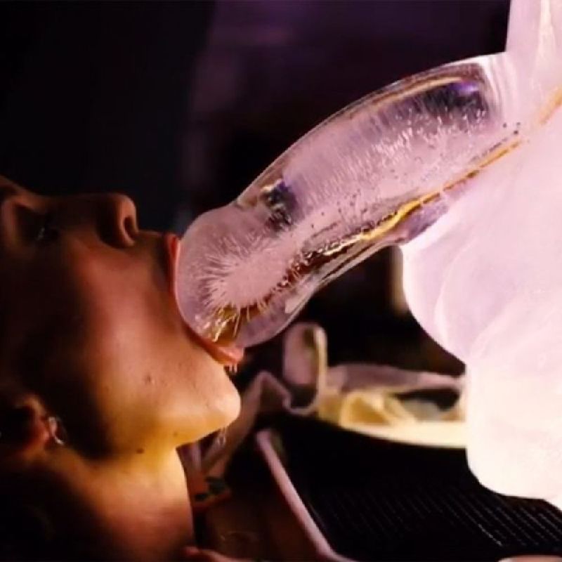 Person enjoying a huge penis ice luge mould filled with beverage for a fun party experience.