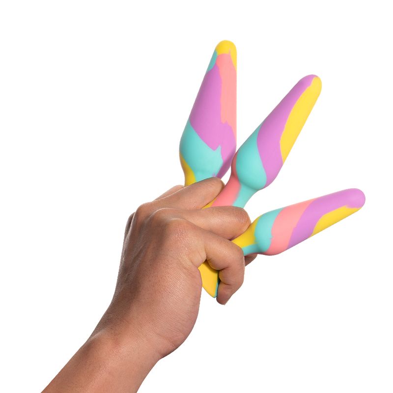 Hand holding TriPlugs 3 Pc Silicone Anal Training Kit featuring colorful silicone design.