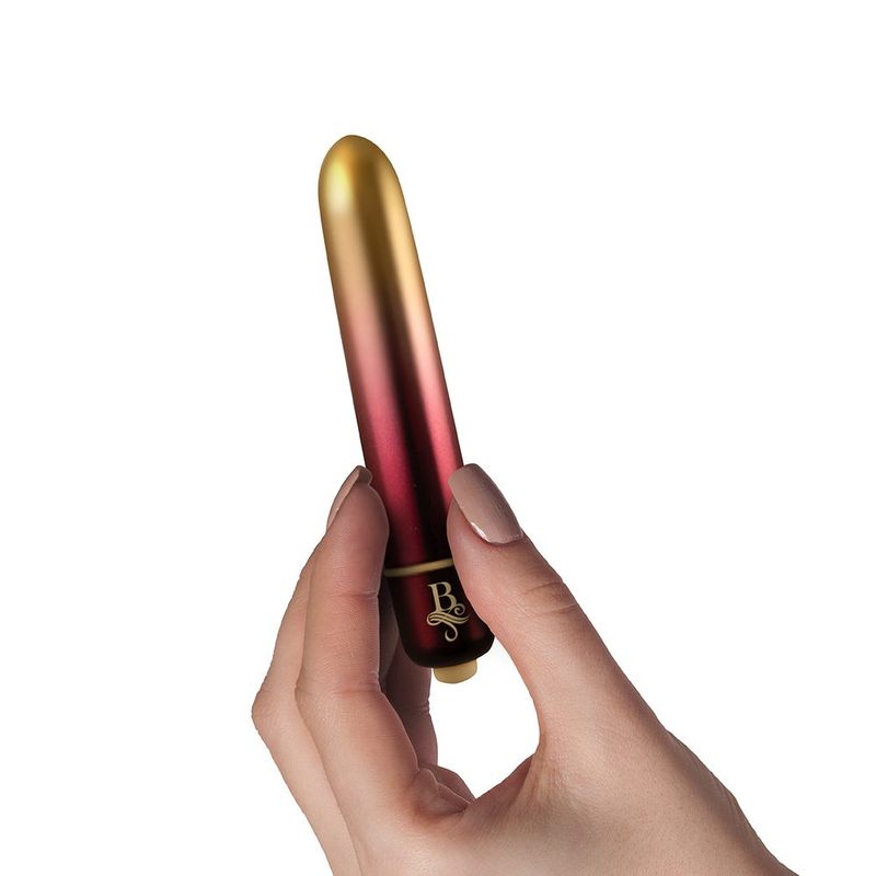 A hand holding a Boudoir Debutante waterproof bullet vibrator with a gold and red finish.
