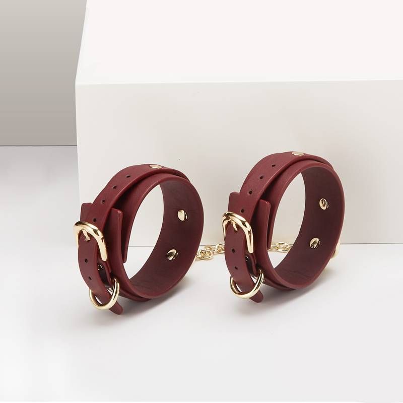 Burgundy wrist restraints from the 8 Pc Deluxe Bondage Play Kit with gold trim and durable chains.