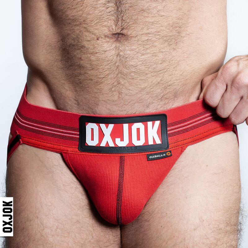 Oxballs Slingjock Upthrust Slider-Strap Jock Black Iron model wearing red jockstrap with bold branding at the waistband.