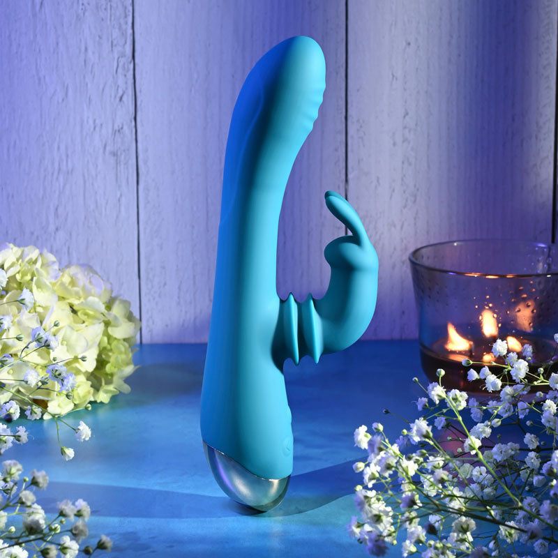 Adam & Eve SHIMMY & SHAKE VELVET RABBIT - 22.4 cm USB Rechargeable Rabbit Vibrator on a surface surrounded by flowers and candles.