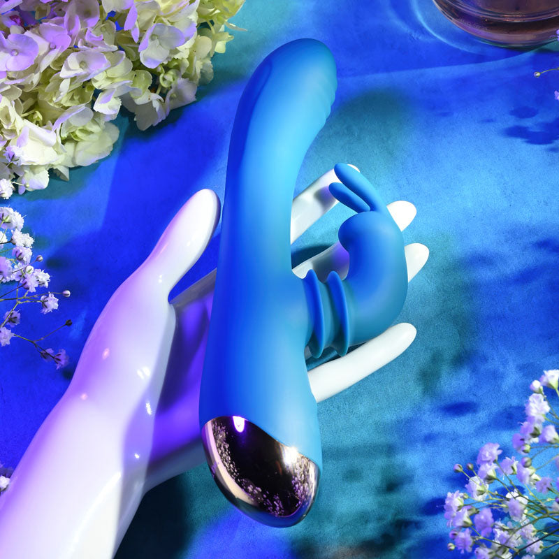 Adam & Eve SHIMMY & SHAKE VELVET RABBIT - 22.4 cm USB Rechargeable Rabbit Vibrator held in a hand surrounded by flowers.