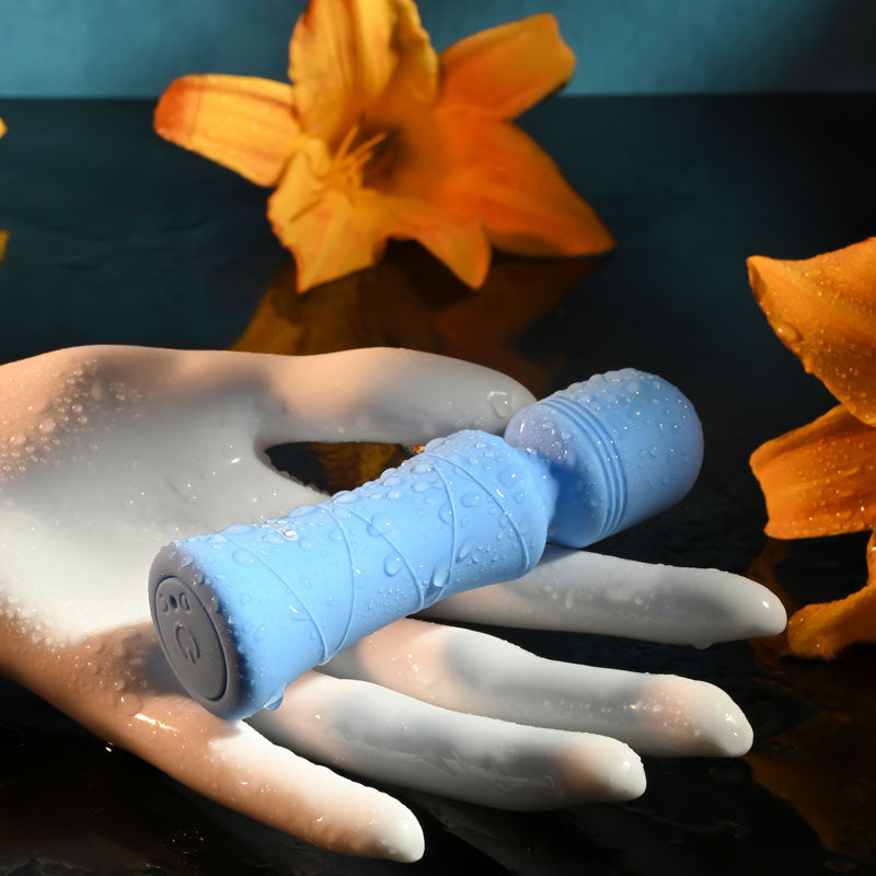 Evolved Out Of The  -  10.5 cm USB Rechargeable Mini Massager Wand resting on a hand surrounded by flowers and water droplets.