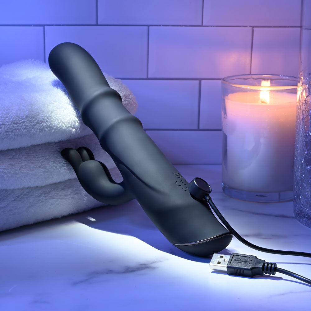 Evolved RINGMASTER - 23.1 cm USB Rechargeable Rabbit Vibrator charging next to candles and towels in a relaxing setting.
