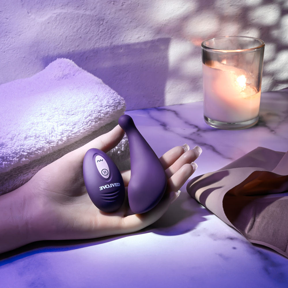 Evolved PANTY PARTY -  USB Rechargeable Panty Vibrator with Remote Control in a hand, relaxed setting with candles.
