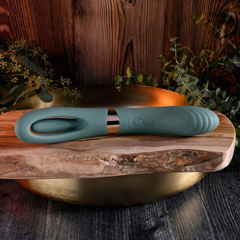 Evolved CHICK FLICK - Olive USB rechargeable vibrator with flicking tip on wooden surface surrounded by greenery.