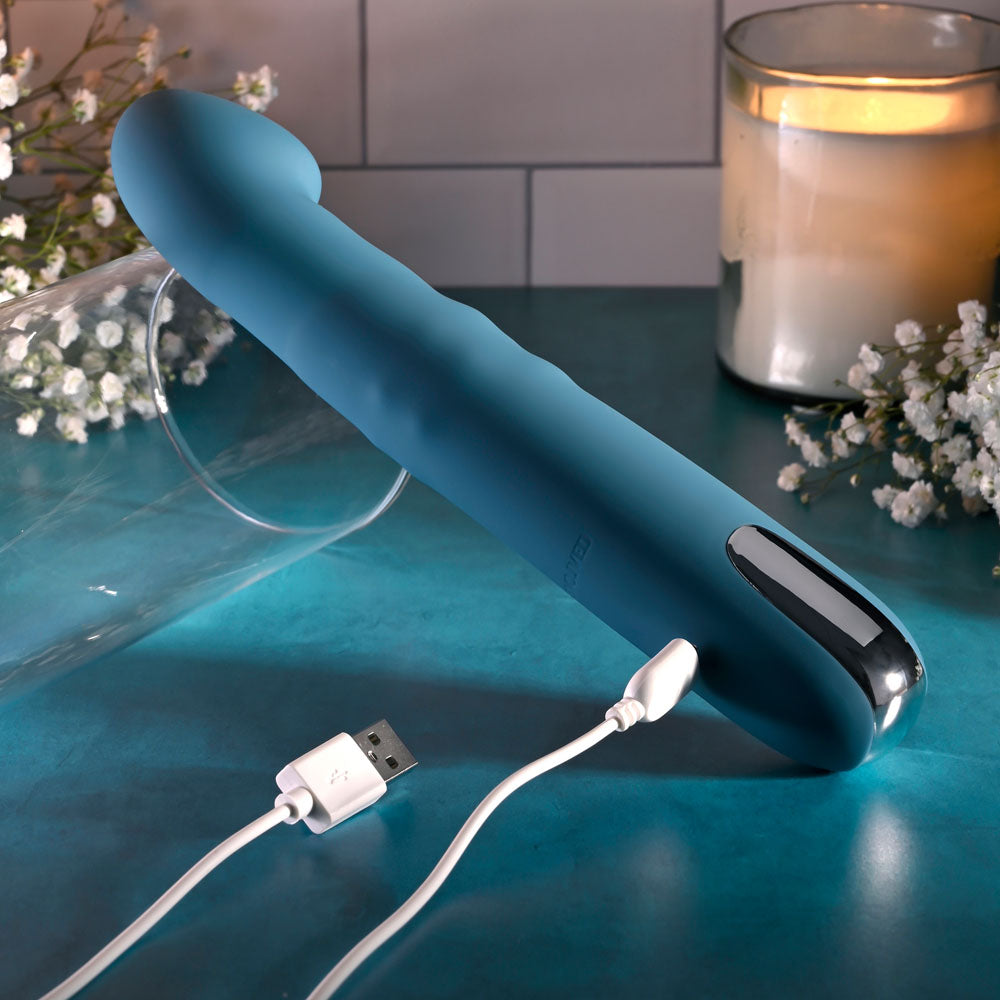 Evolved QUEEN OF ALL TRADES - 22.6 cm USB Rechargeable Thrusting & Rotating Vibrator on a teal surface with charging cable.
