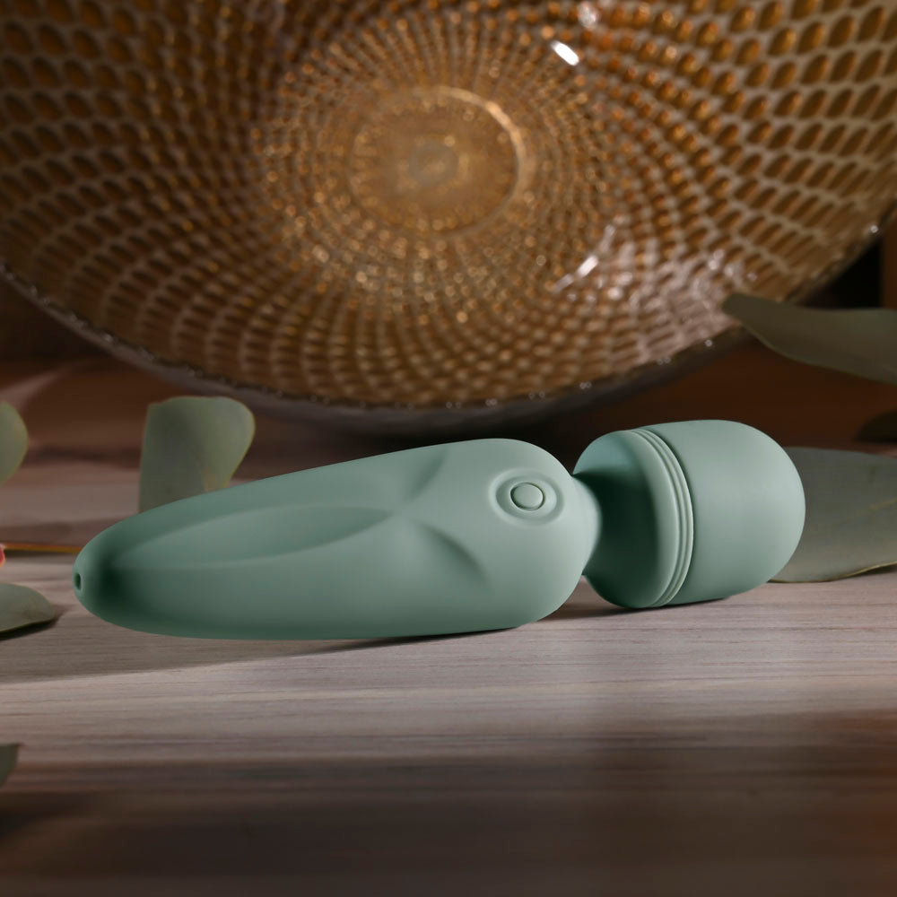 Evolved RUMBLE WAND - Olive  13.4 USB Rechargeable Mini Massage Wand on a wooden surface with greenery.