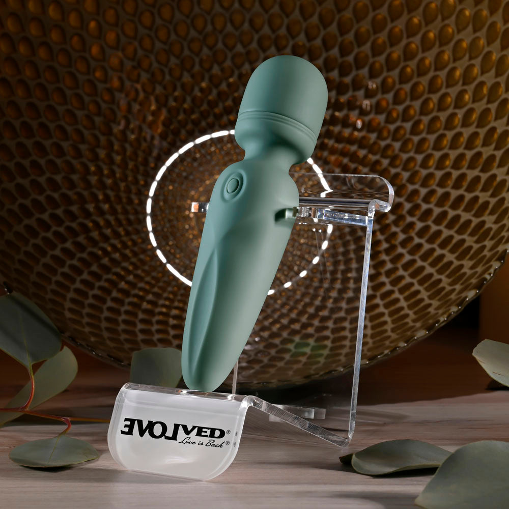 Evolved RUMBLE WAND - Olive  13.4 USB Rechargeable Mini Massage Wand displayed on a clear stand with a textured backdrop.