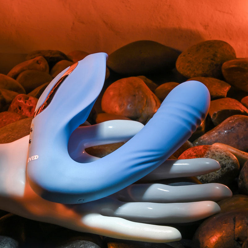 Evolved TAP & THRUST - USB Rechargeable Dual Vibrator resting on a hand among smooth stones, showcasing its sensual design.