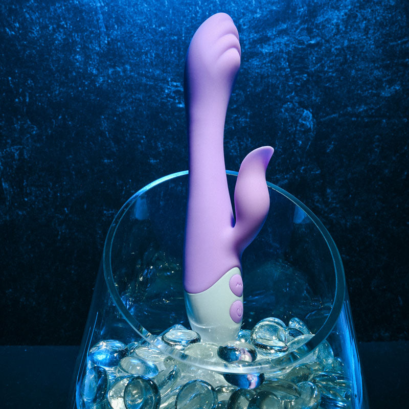 Evolved PLEASING PETAL - Lilac 19.7 cm USB Rechargeable Rabbit Vibrator displayed elegantly on decorative stones.