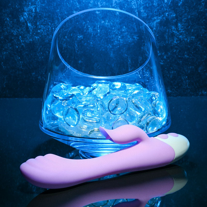 Evolved PLEASING PETAL - Lilac 19.7 cm USB Rechargeable Rabbit Vibrator next to decorative glass stones.