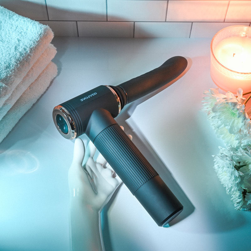 Evolved TOO HOT TO HANDLE - USB Rechargeable Thrusting Vibe with Stand on a bathroom counter, next to candles and towels.