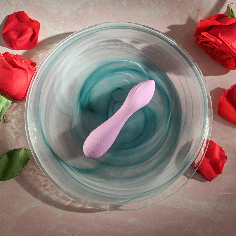 Evolved LILAC G - Lilac 11.5 cm USB Rechargeable Mini Vibrator resting in a bowl, surrounded by rose petals.