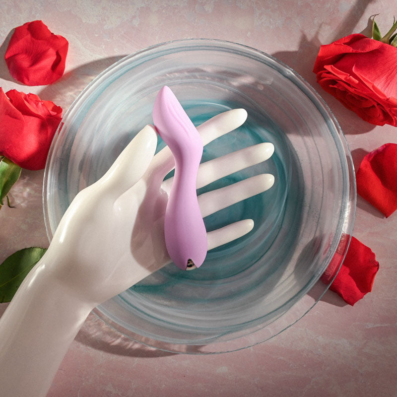 Evolved LILAC G - Lilac 11.5 cm USB Rechargeable Mini Vibrator resting in a hand above a bowl and surrounded by roses.