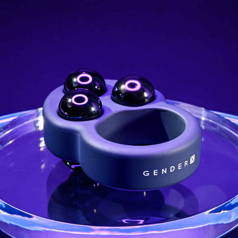 Gender X WORKOUT RING -  Weighted Cock Ring on a clear surface with three removable steel balls for enhanced play.