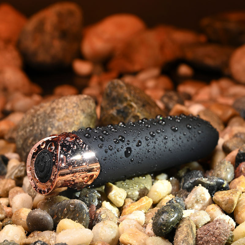 Gender X THE GOLD STANDARD - /Rose Gold 10 cm USB Rechargeable Bullet on wet stones, showcasing its sleek design.