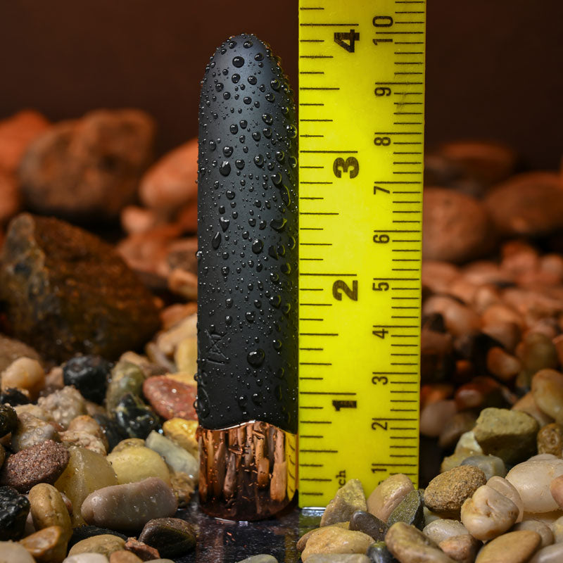 Gender X THE GOLD STANDARD - /Rose Gold 10 cm USB Rechargeable Bullet next to a ruler among decorative pebbles.