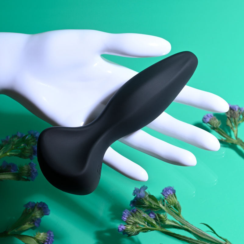 Gender X HIP TO BE SQUARE - black silicone toy resting on a hand with flowers.