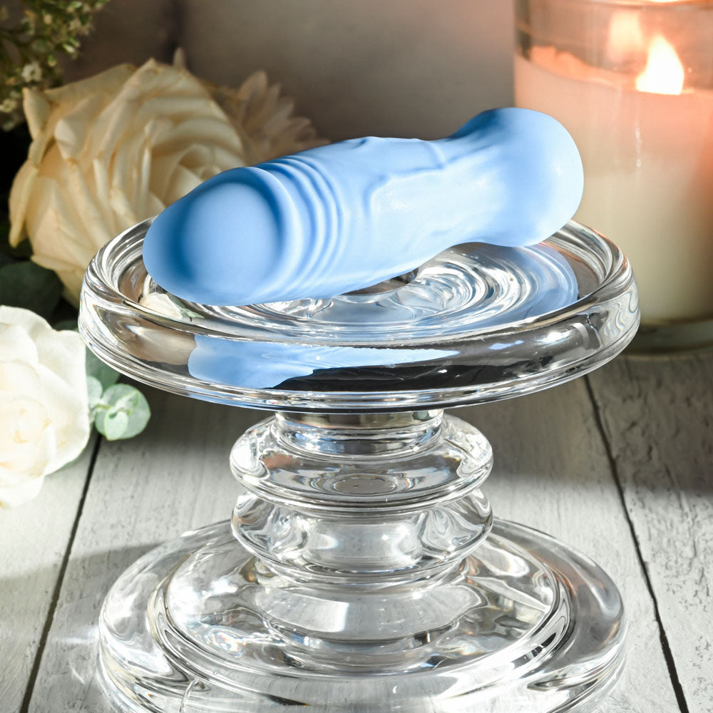 Gender X LIL BUDDY - Light 10.1 cm USB Rechargeable Mini Vibrator on a glass pedestal with flowers and candle.