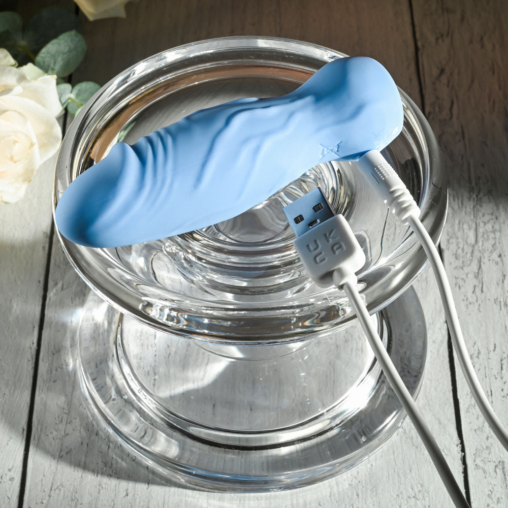 Gender X LIL BUDDY - Light 10.1 cm USB Rechargeable Mini Vibrator in blue on a glass plate.