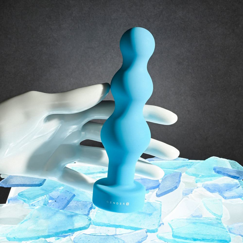 Gender X PLUGGED UP - 13.6 cm USB Rechargeable Butt Plug held against a backdrop of blue glass pieces.