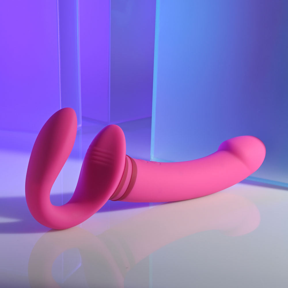 Gender X rechargeable strap-on vibrator in vibrant pink, showcasing its dual-ended design and sleek silhouette.