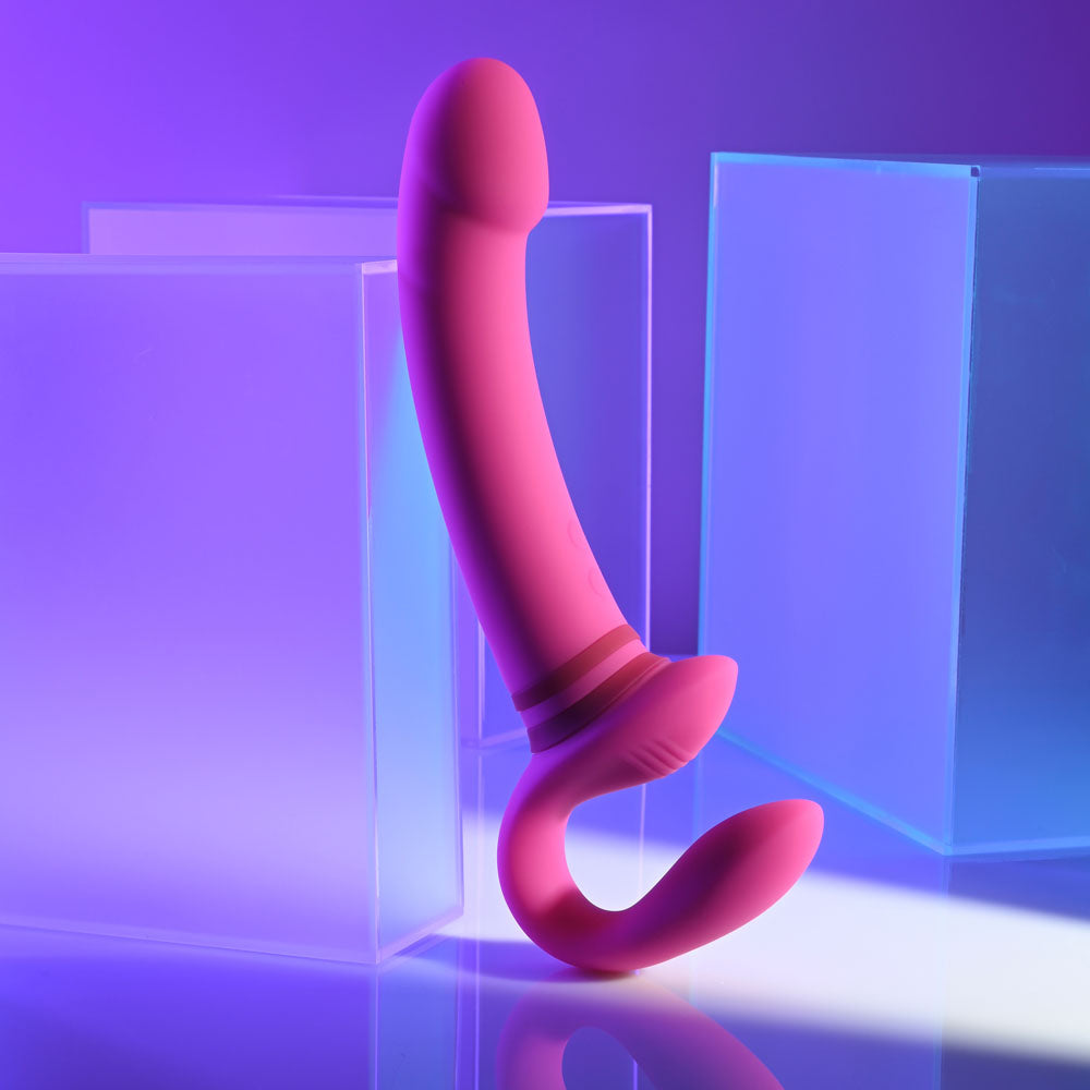 Gender X rechargeable strap-on vibrator in pink against colorful background with transparent blocks.