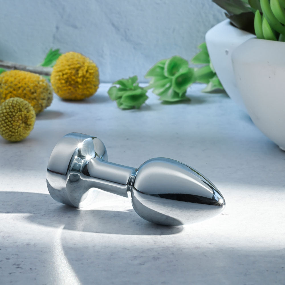 Gender X ROCKIN METAL PLUG MINI -  7.8 cm USB Rechargeable Vibrating Mini Butt Plug on a surface with green plants.