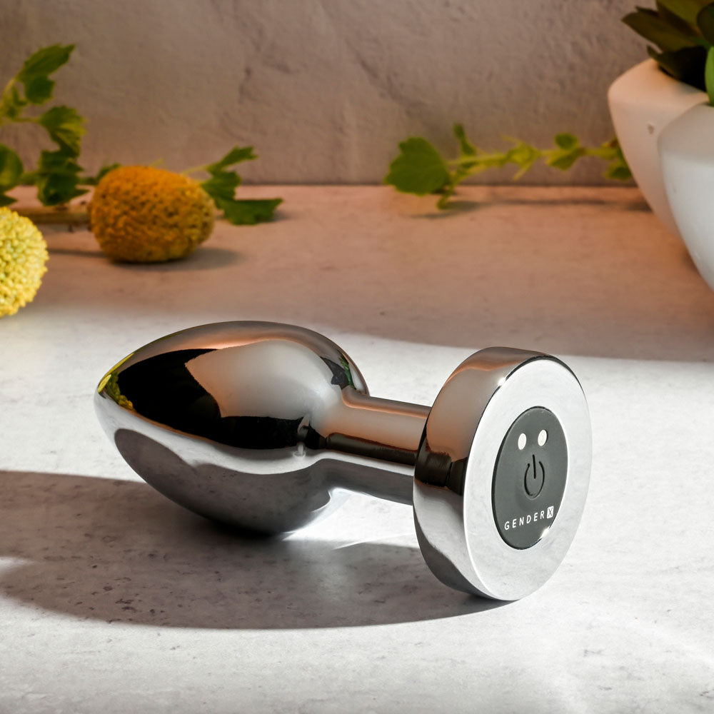 Gender X ROCKIN METAL PLUG XL - 10.5 cm USB Rechargeable Vibrating XL Butt Plug on a countertop with flowers.