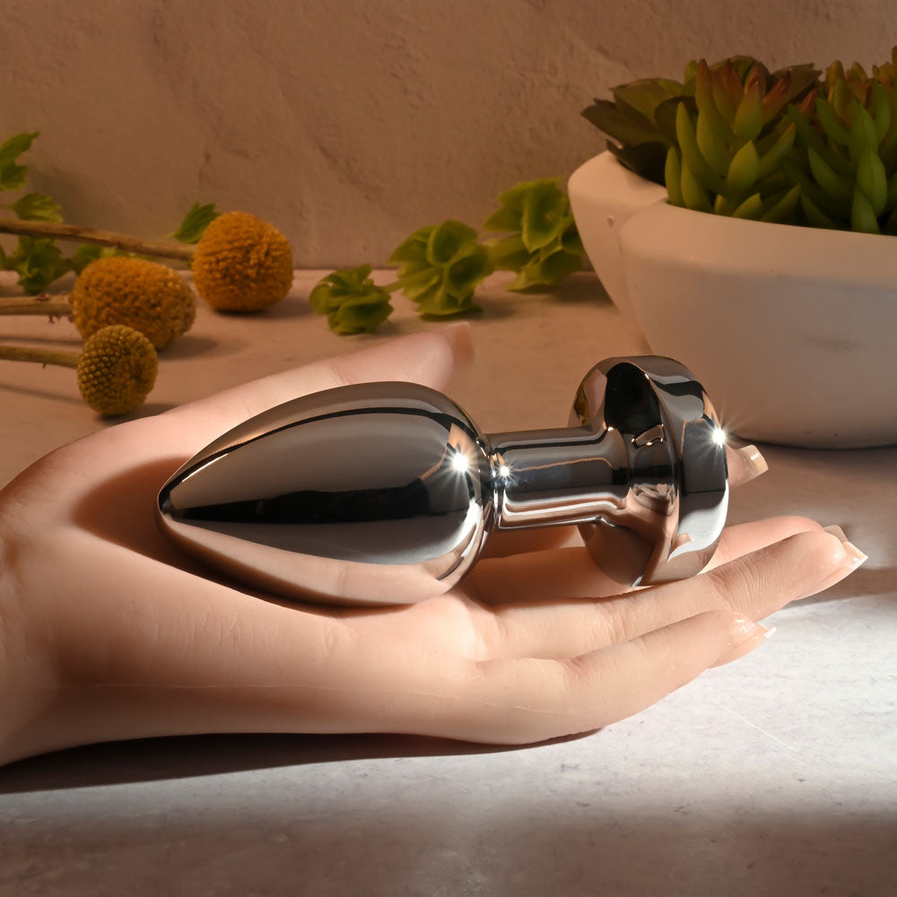 Gender X ROCKIN METAL PLUG XL -  10.5 cm USB Rechargeable Vibrating XL Butt Plug in a hand with elegant decor.