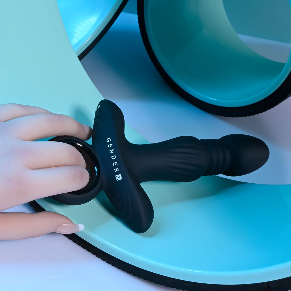 Gender X SLAYER rechargeable thrusting vibrating butt plug being held, showcasing its sleek design and textured grip.