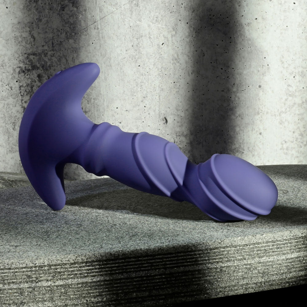 USB rechargeable vibrator with remote in purple laying on a stone surface.