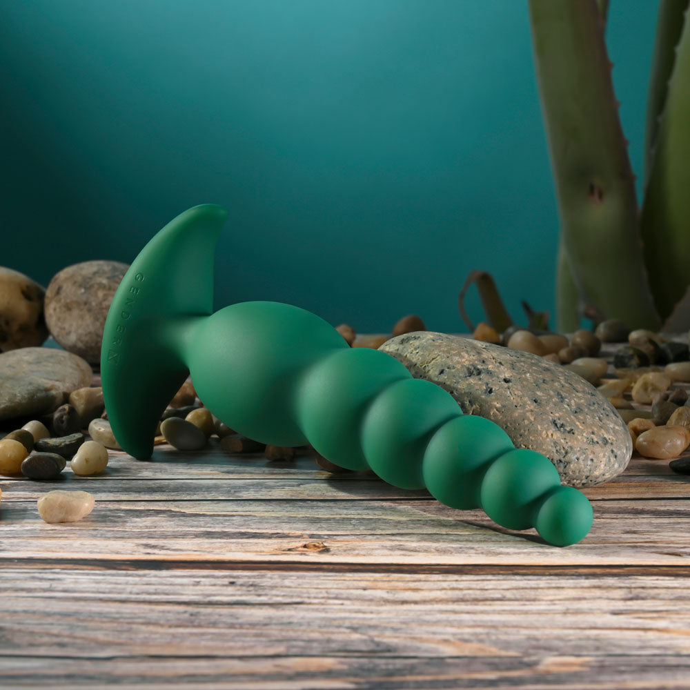 Gender X THE RATTLER - 17 cm USB rechargeable vibrating anal plug on a wooden surface with stones.