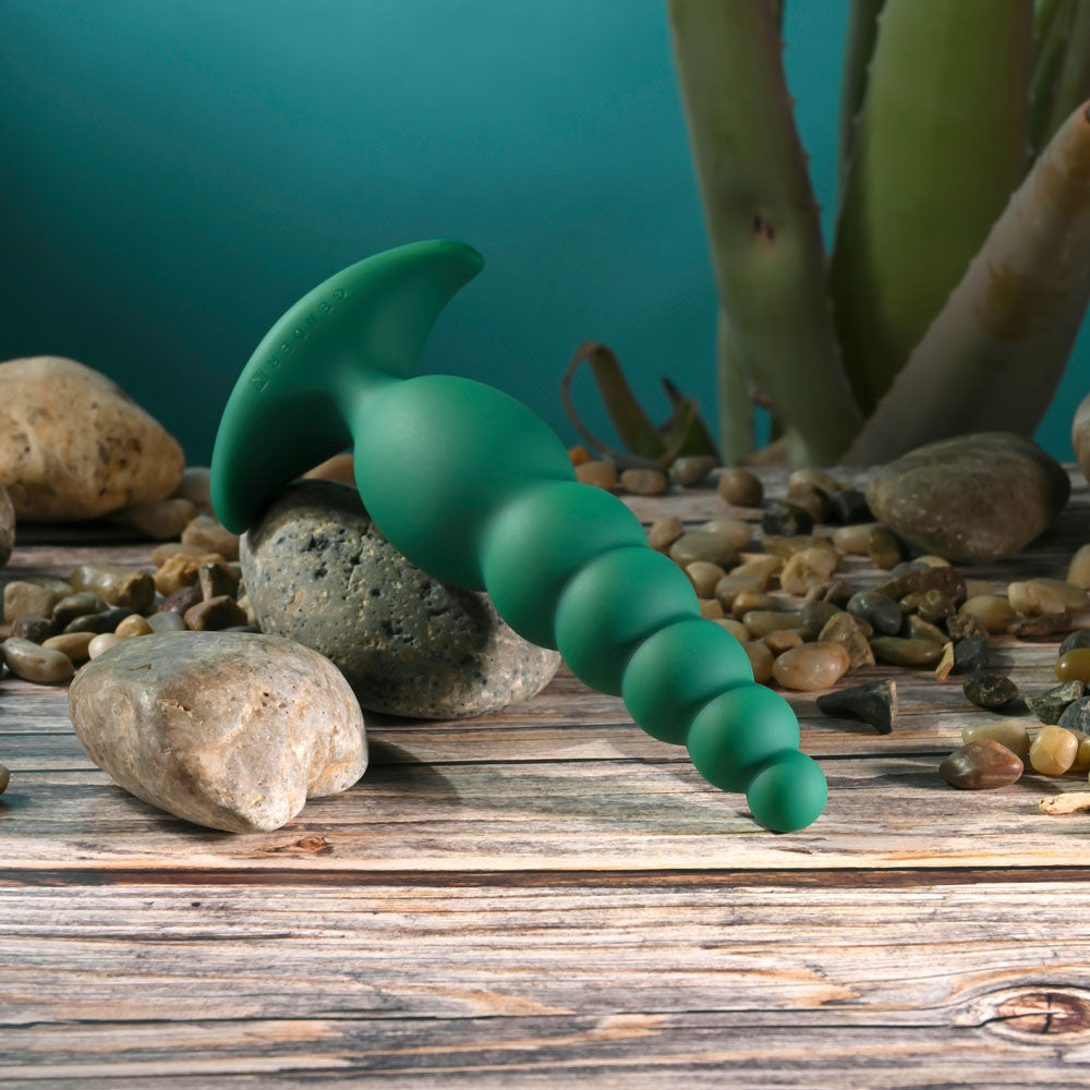 Gender X THE RATTLER -  17 cm USB Rechargeable Vibrating and Twirling Anal Plug on a wooden surface with stones.