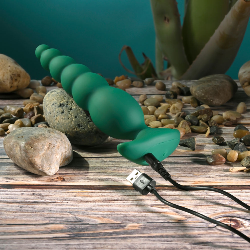 Gender X THE RATTLER -  17 cm USB Rechargeable Vibrating and Twirling Anal Plug charging on a wooden surface.