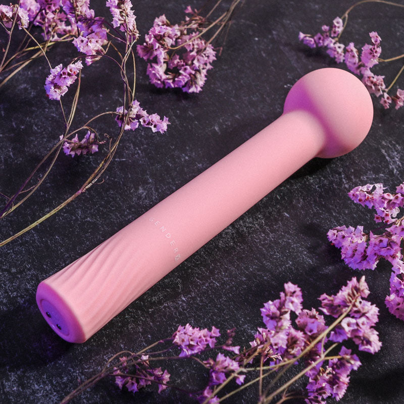Gender X FLEXI WAND - 16.6 cm USB Rechargeable Vibrator surrounded by pink flowers on a dark background.