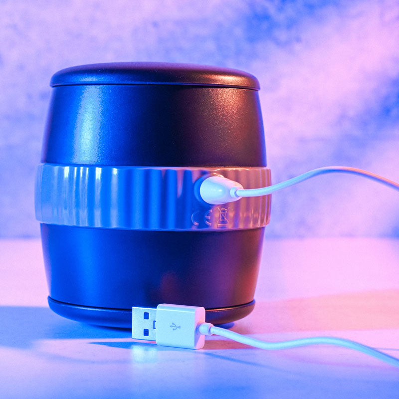 Gender X BARREL OF FUN - USB Rechargeable Stroker on a surface with USB cable connected.