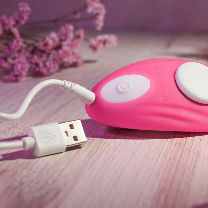 Gender X UNDER THE RADAR -  USB Rechargeable Panty Vibe charging on a wooden surface with pink flowers in the background.