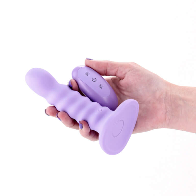 Purple wireless rechargeable vibrating dildo with ribbed shaft and remote control in hand.