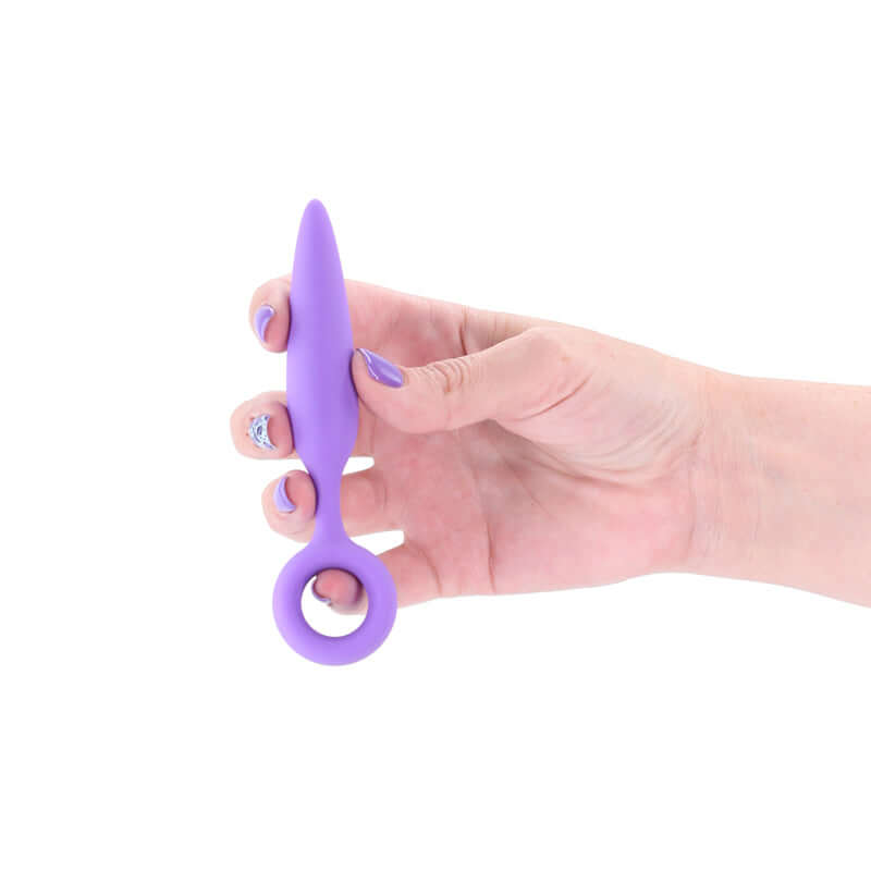Purple silicone beginner anal plug held in a hand, featuring a tapered design and finger rings for control.