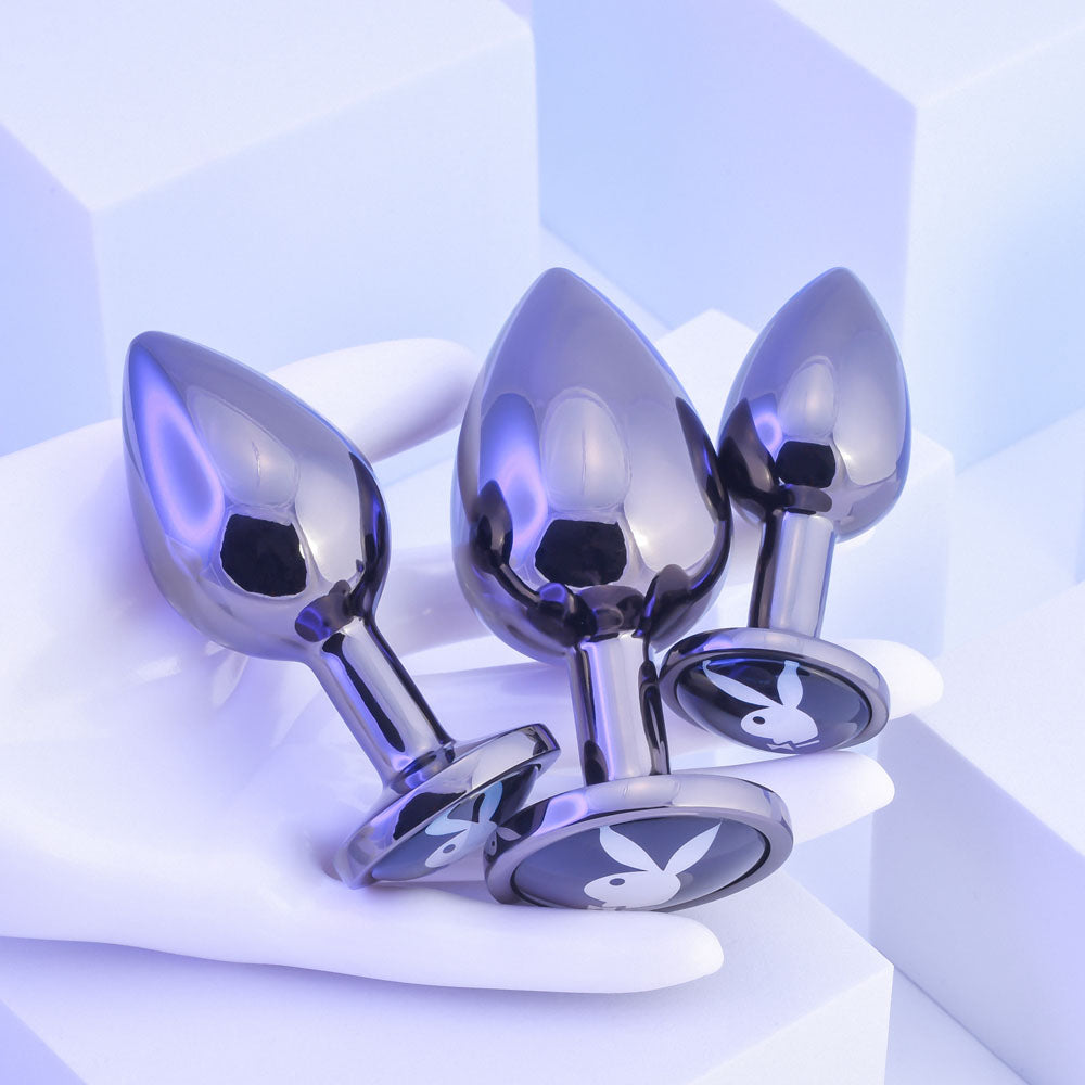 Playboy Pleasure PLEASURE 3 WAYS - Metal Butt Plugs - Set of 3 Sizes displayed on a hand, showcasing their sleek design and flared bases.