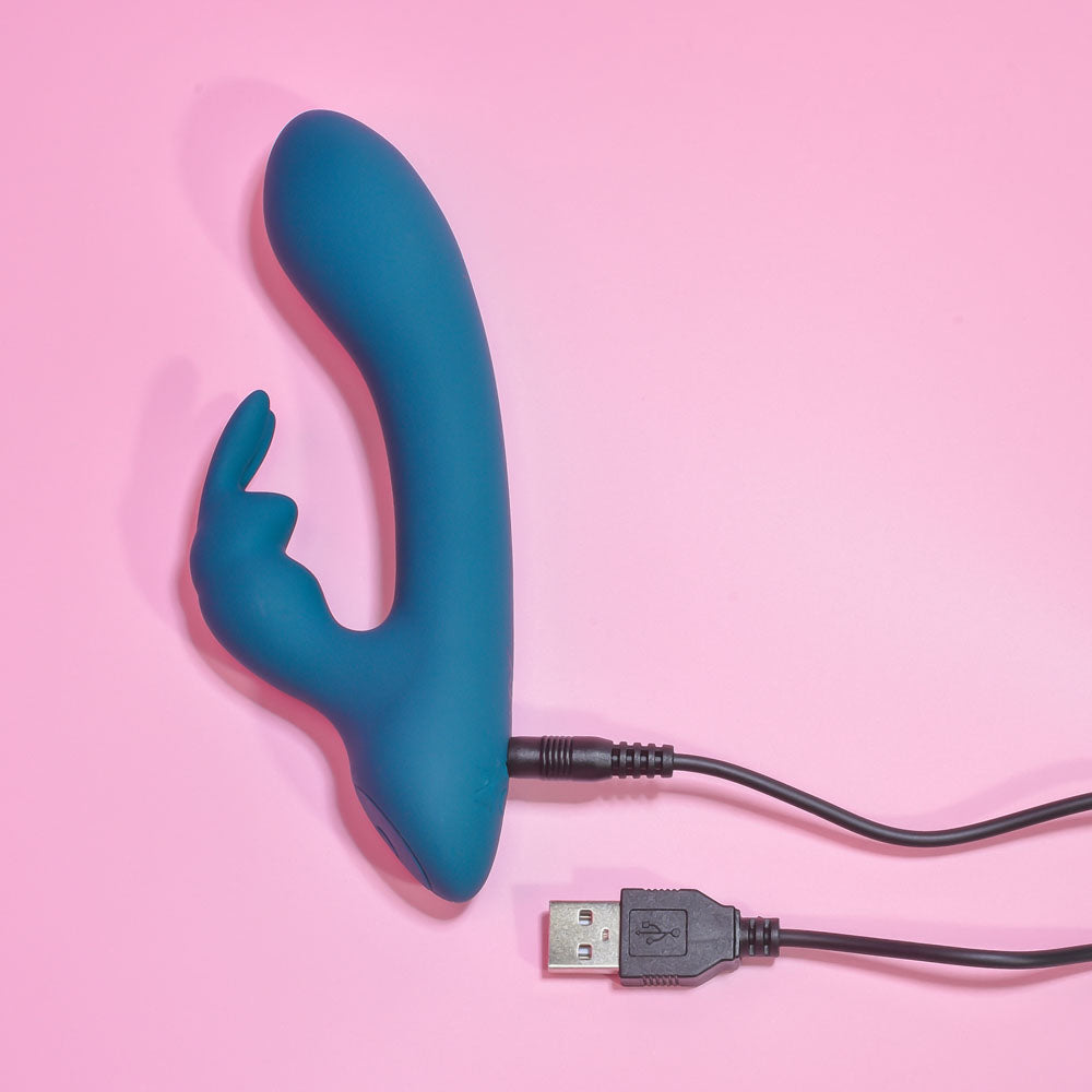 Playboy Pleasure LIL RABBIT - Deep Teal 14.6 cm USB Rechargeable Rabbit Vibrator on pink background, charging.
