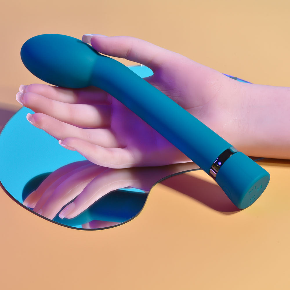 Hand holding a blue G-Spot vibrator on a mirrored surface, showcasing its sleek design and oval head for pleasure.