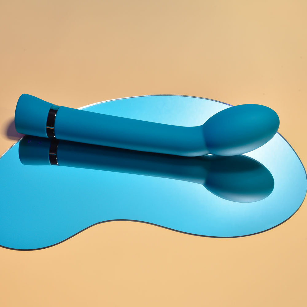 G-Spot vibrator in blue silicone on mirrored surface, showcasing sleek design and oval head for precise stimulation.