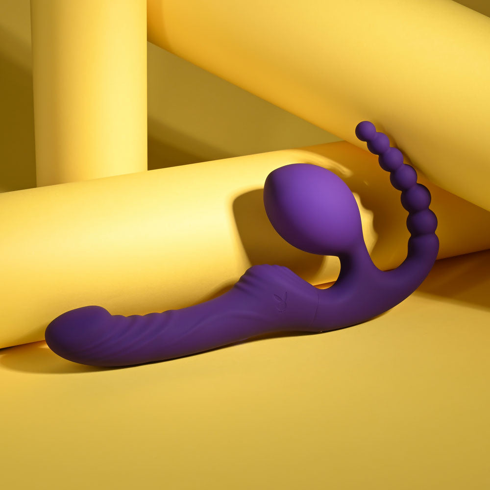 Playboy Pleasure HUG IT OUT - 29 cm USB Rechargeable Strapless Strap-On in vibrant purple against a yellow backdrop.