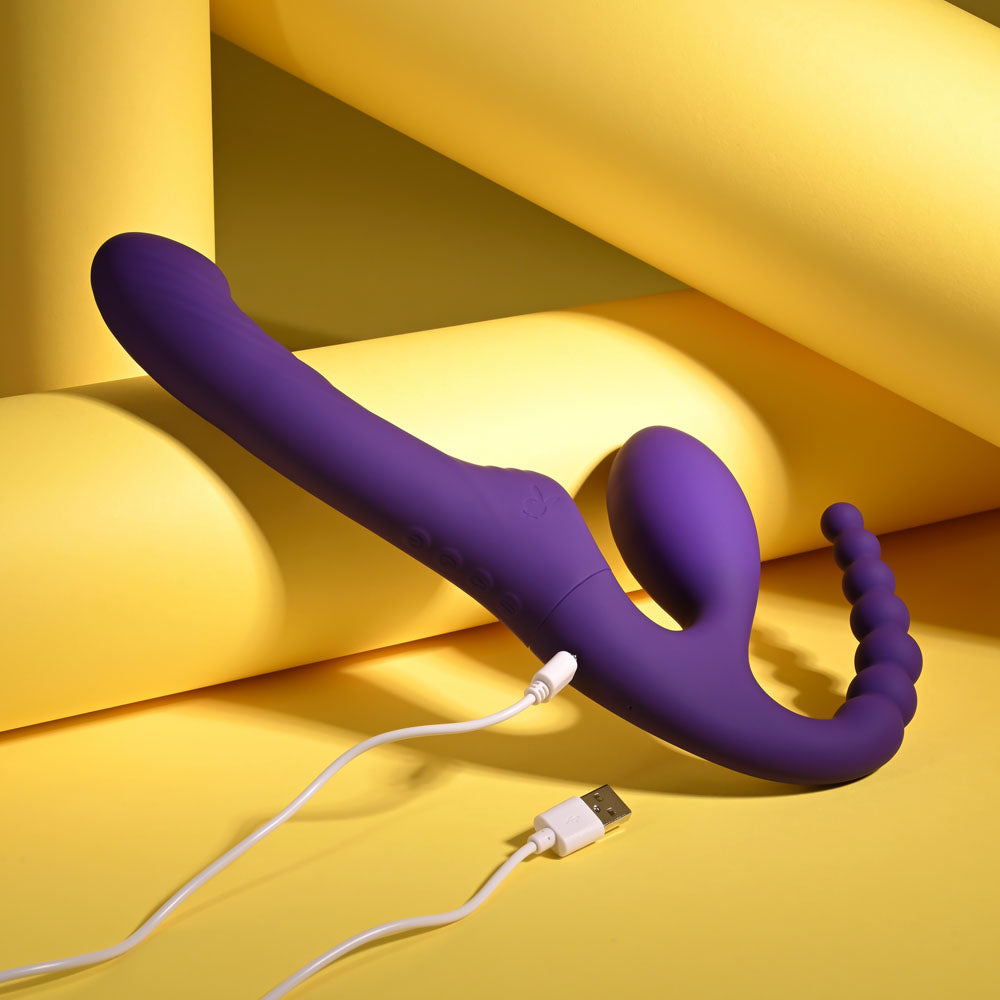 Playboy Pleasure HUG IT OUT - 29 cm USB Rechargeable Strapless Strap-On in purple against a yellow background.