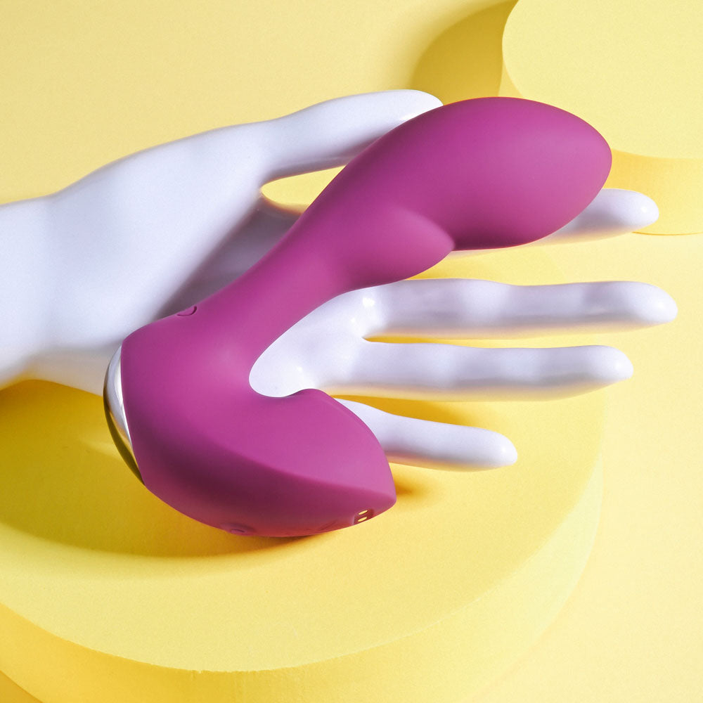 Playboy Pleasure ARCH - 14.1 cm USB Rechargeable G-Spot Vibrator on a hand against a yellow background.