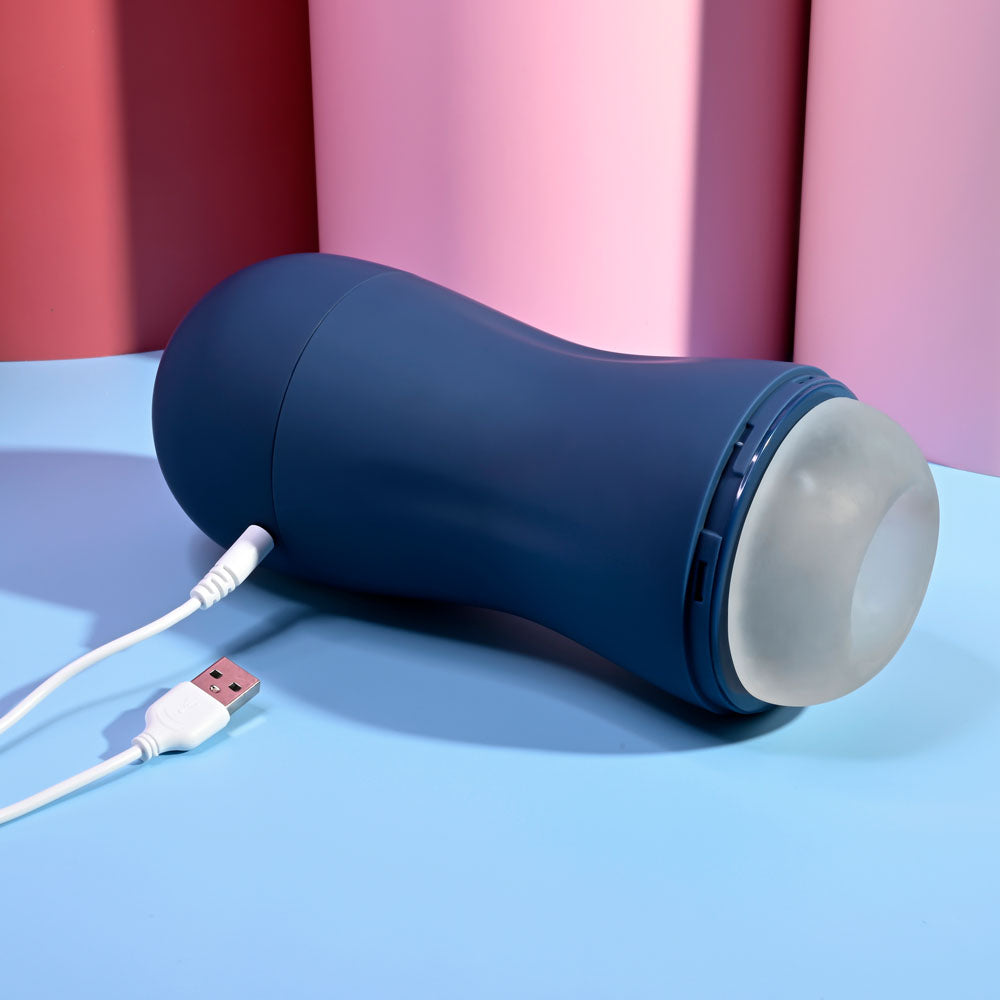 Playboy Pleasure GUSTO - USB Rechargeable Vibrating & Sucking Masturbator charging on a blue surface with a USB cable.
